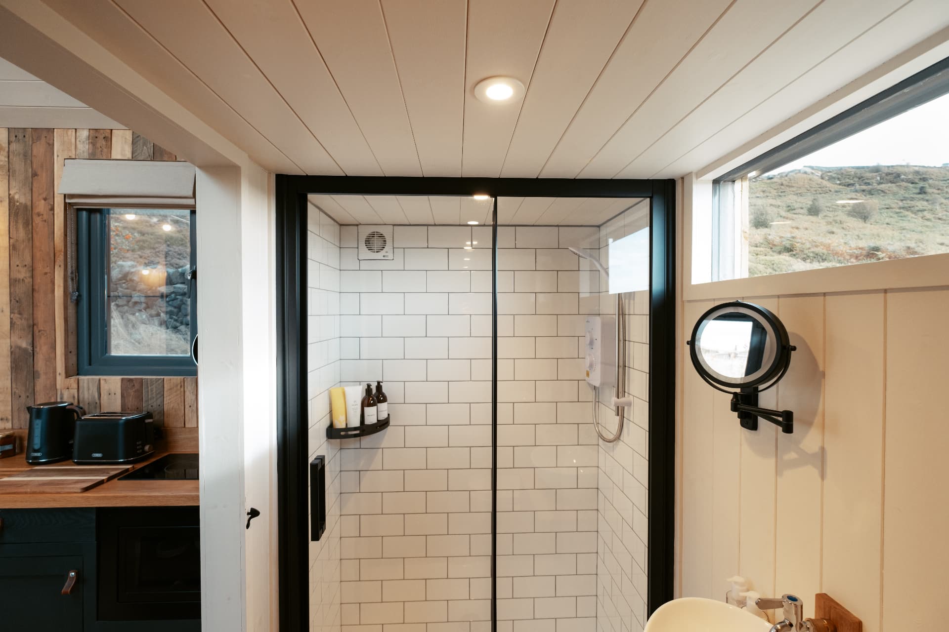 The walk-in shower in The Bothy, white tiled with a window over the hillside
