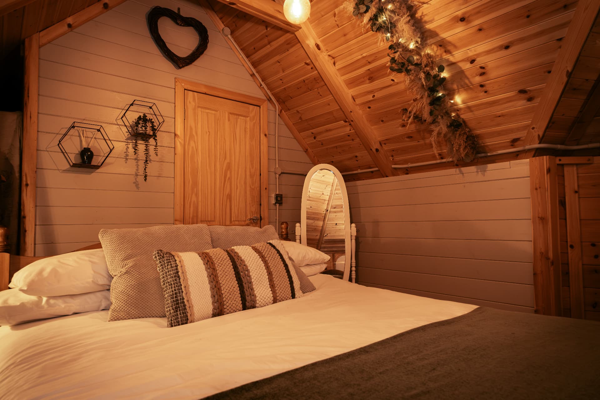 Candlelit bedroom inside The Mallard with a woven heart above the bed and fairy lights along the beams