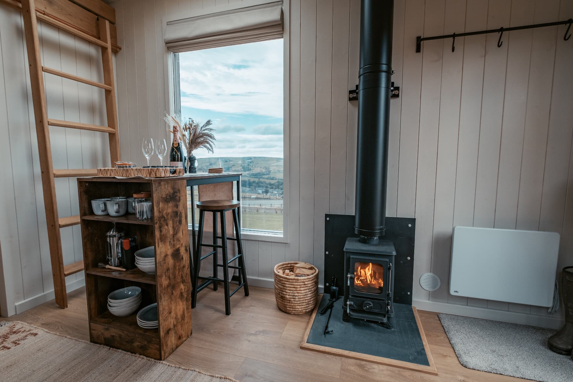 The wood-burning stove and breakfast bar in The Bothy, with champagne on the bar and the valley through the window