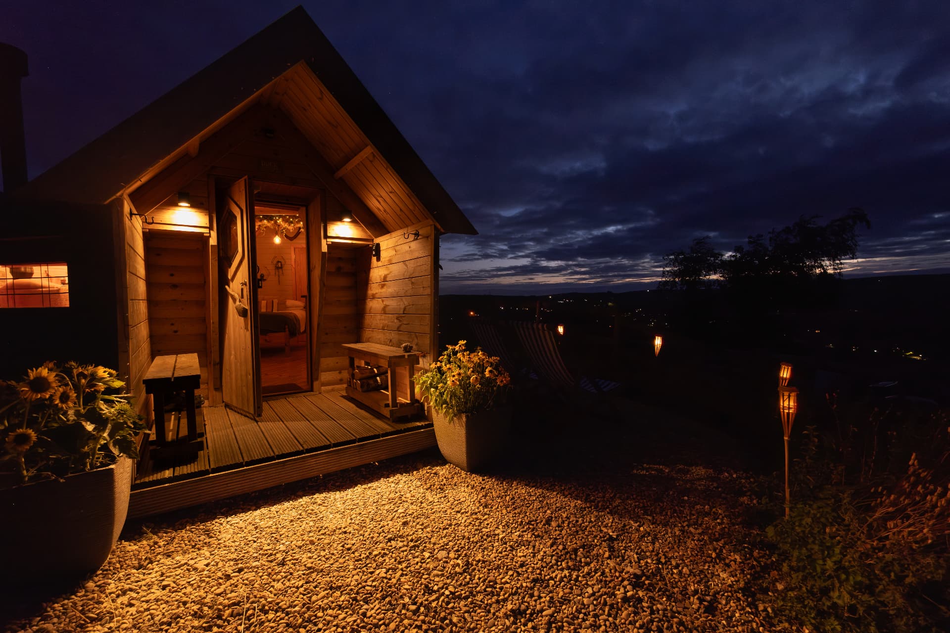 The cabin lit warmly at nightfall with flame torches and sunflowers outside