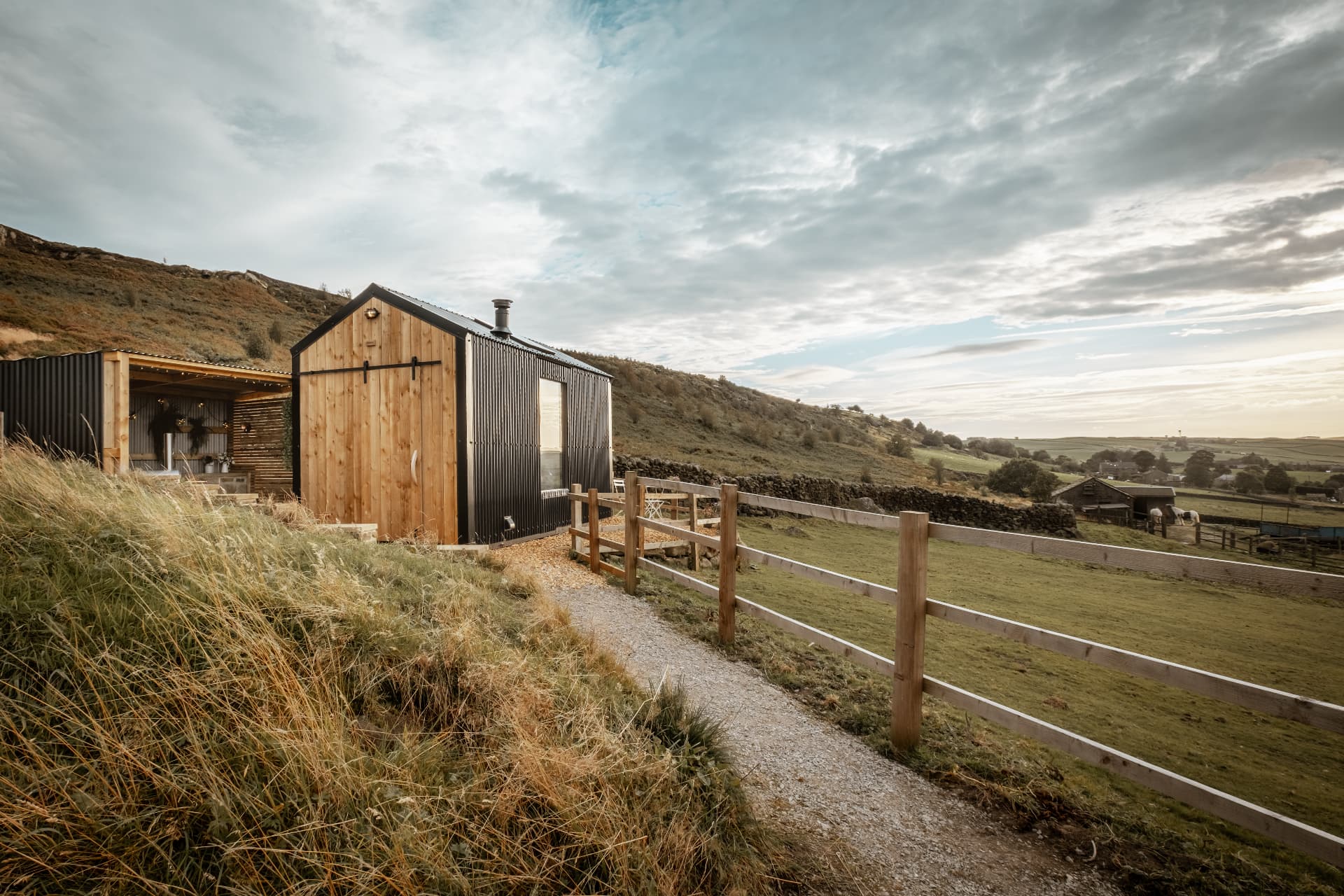 The Bothy on its hillside track, with the covered pizza-oven shelter beside it and the valley beyond